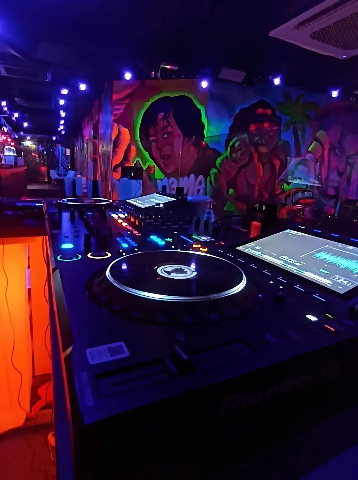 The DJ booth under UV light with a neon portrait mural